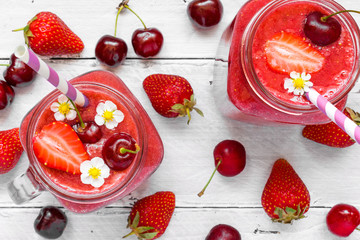 strawberry and cherry smoothie in glass jars with straw and fresh fruits and berries