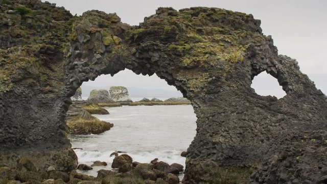 Wide panning shot of waves on beach near arch rock formation. Arnarstapi, Snaefellsnes, Iceland