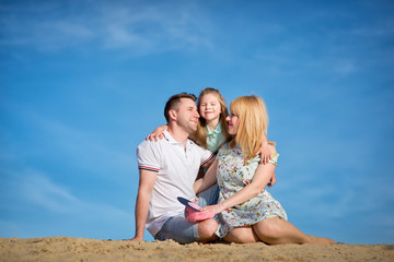 Fototapeta na wymiar Happy beautiful laughing family sitting on the sand on the beach against the background blue sky in summer vacation.