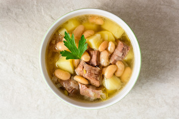 Beef soup with potatoes, beans and leeks in ceramic bowl on stone background.