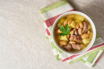 Beef soup with potatoes, beans and leeks in ceramic bowl on stone background.