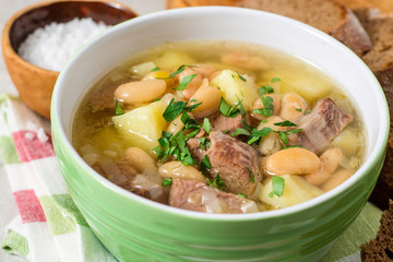 Beef soup with potatoes, beans and leeks in ceramic bowl on stone background.