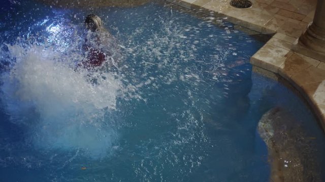Medium high angle shot of man in shirt and tie jumping in pool. Cedar Hills, Utah, United States