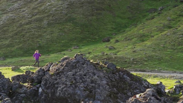 Wide slow motion tracking shot of woman running on mountain path. Iceland