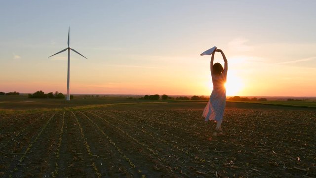 Beautiful young woman enjoying nature at sunset against the background of a windmill.