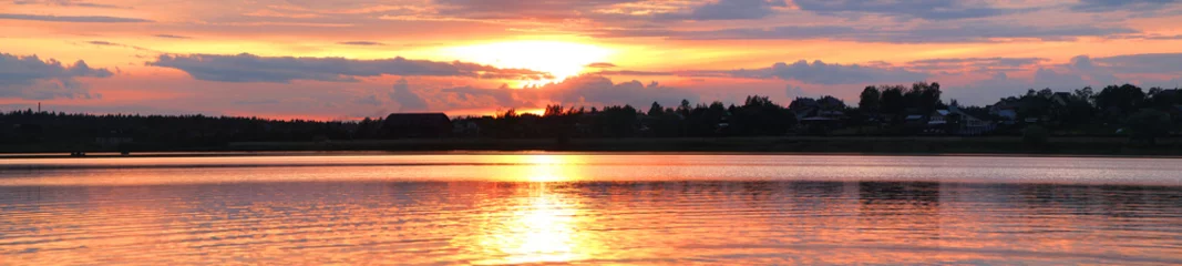 Panorama of the sunset overlooking the lake and the house and trees on the opposite coast. © blackguitar1