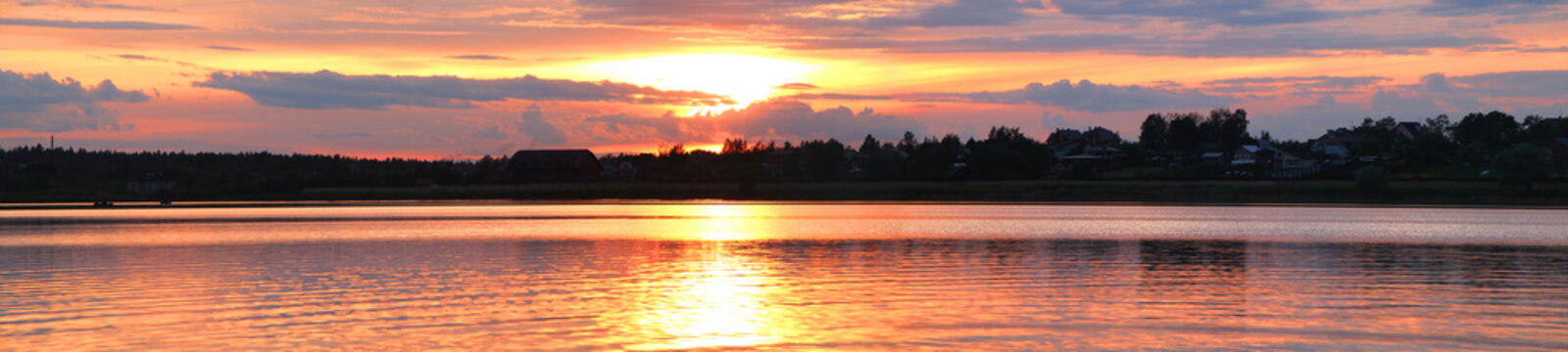 Panorama of the sunset overlooking the lake and the house and trees on the opposite coast.