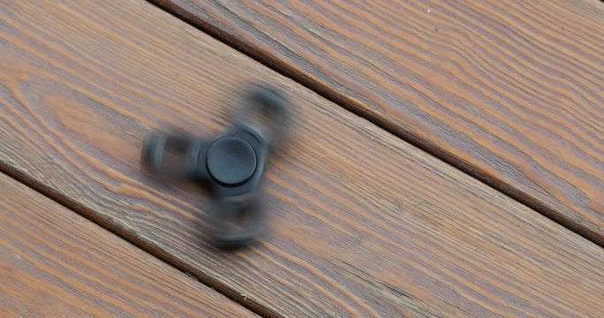 hand spinner, or fidgeting spinner, rotating on the floor. wooden background.
