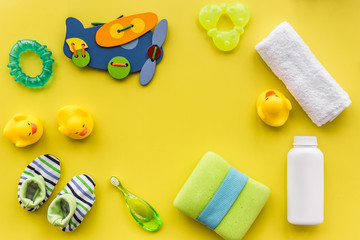 Baby care accessories, toys and clothing on yellow background top view mock up