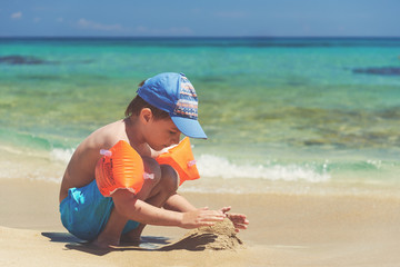 Boy in floating sleeves on a beach with transparent water.
