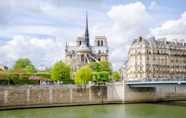 Notre Dame de Paris Catholic Christian Cathedral with the Seine river, a bridge and typical parisian buildings on a sunny spring day