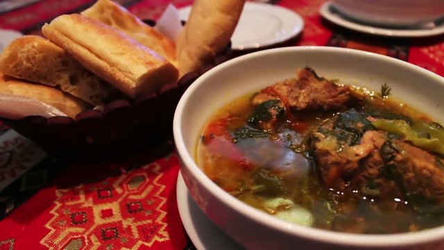 Delicious national Azerbaijani lamb soup in restaurant. Bouillon of meat in a white plate on a background of bread tortillas