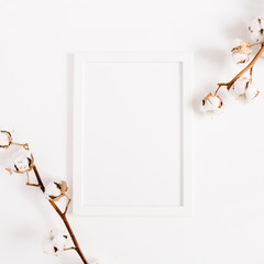 White blank photo frame mock up and cotton branches on white background. Flat lay, top view.