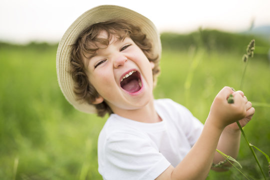 Portrait of adorable kid boy with hat standing on a summer meadow