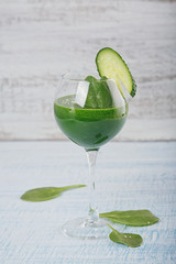 Green spinach and cucumber smoothie on light blue wooden background.