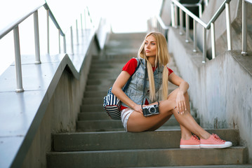 Young beautiful sexy fashionable hipster girl in shorts is resting sitting on the ground and taking pictures. The concept of lifestyle