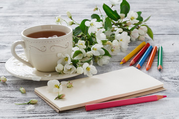 blank greeting card and cup of green flower tea with branches of blossoming cherry on white rustic wooden background