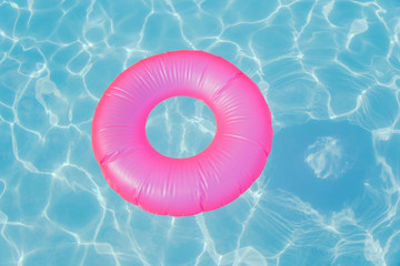 Bright pink float in blue swimming pool, ring floating in a refreshing blue swimming pool with waves reflecting in the summer sun. Active vacation background. Lifesaver for kid. Sunny day at the pool.
