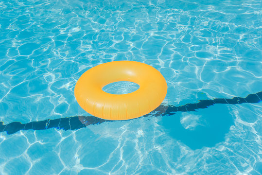 Bright orange float in blue swimming pool, ring floating in a refreshing blue swimming pool with wave reflecting in the summer sun. Active vacation background, lifesaver for kid. Sunny day at the pool