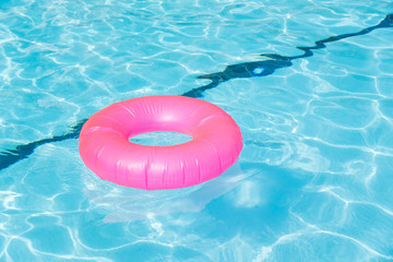 Bright pink float in blue swimming pool, ring floating in a refreshing blue swimming pool with waves reflecting in the summer sun. Active vacation background. Lifesaver for kid. Sunny day at the pool.