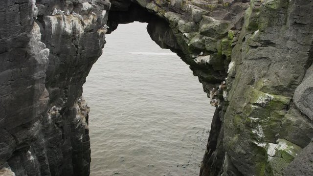 Wide crane shot of birds flying near arch rock formation. Arnarstapi, Snaefellsnes, Iceland