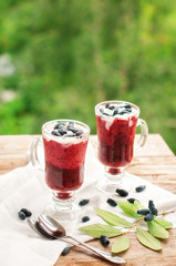 glass of smoothies with berries and ice cream on wooden table with spoon and leaves