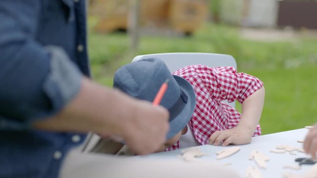 Little boy wearing is watching at his father screwing a wooden plane