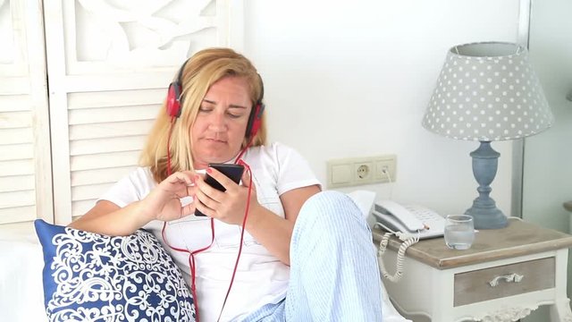 Portrait of a blonde attractive woman with headphone listening to music and relaxing at the bedroom