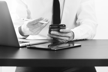 close up of businessman working with smart phone on wooden desk in modern office,black and white