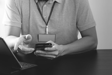 businessman in pink t-shirt working with smart phone and digitl tablet computer on wooden desk in modern office,black and white