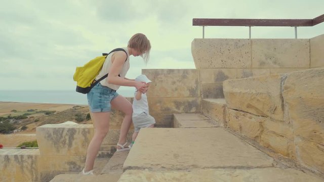 Caring young mom holding her son, helps baby to climb the steps of the stairs. Family of tourists mom and son climb the steps, architectural monument.