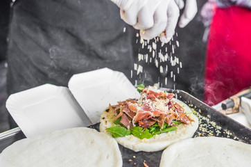 Chef preparing tortilla with arugula, parma jamon ham, and parmesan cheese at a street food market