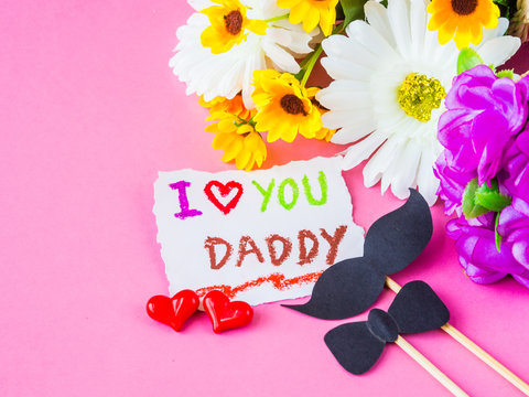 Father's day concept. I LOVE YOU DADDY message with white and yellow flower, two red heart and black Mustache on pink background