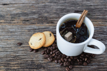 Brown sugar cube falling  into hot coffee mug with coffee beans and cookies on wood background