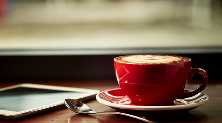Red cup of cappuccino with beautiful latte art on old wooden background