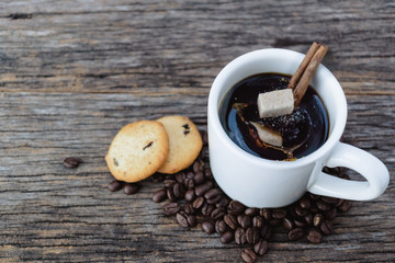 Brown sugar cubes falling  into hot coffee mug with coffee beans and cookies on wood background