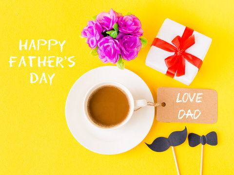 Father's day concept. Happy Father's Day and LOVE DAD message with pink flower, coffee cup, white gift and black Mustache on yellow background