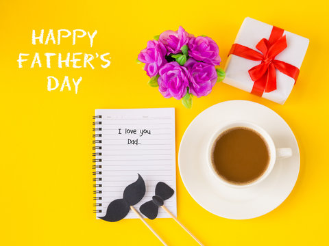 Father's day concept. Happy Father's Day and I LOVE DAD message on note book with pink flower, coffee cup, white gift and black Mustache on yellow background