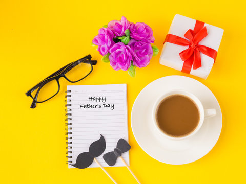 Father's day concept. Happy Father's Day and I LOVE DAD message on note book with pink flower, coffee cup, white gift and black Mustache on yellow background