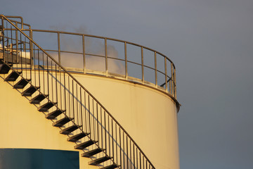 Metal staircase on the oil tank lit by the evening sun.