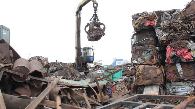 Sorting and loading of scrap metal. / Excavator is loading scrap metal junk into a bin at a garbage dump or recycling center.