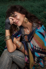 Beautiful boho woman wearing poncho sitting on green field © zolotareva_elina