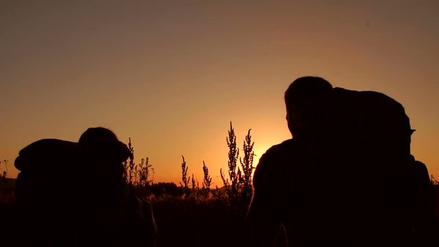 Silhouette of a couple of tourists with hiking backpacks ascending to the top of the mountain at sunset, slow motion.