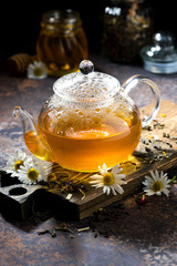 fragrant chamomile tea in a glass teapot on dark background, vertical