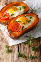 Tasty baked sweet potato stuffed with fried egg and tomato close-up. vertical
