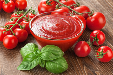 Bowl with ketchup basil and tomatoes on a wooden background.