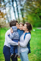 Fototapeta premium Family, mom, dad and younger child escort the eldest girl to school for the first time. Parents hold the daughter in her arms and kiss her at the same time