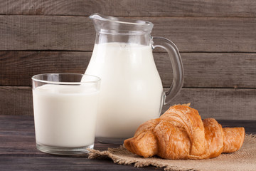 jug and glass of milk with croissant on a wooden background
