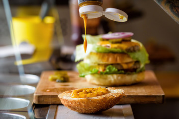 Making Delicious Homemade Maxi Burger with grilled beef steak, lettuce, cheese, tomato, onion, barbecue sauce, honey mustard, pickles
