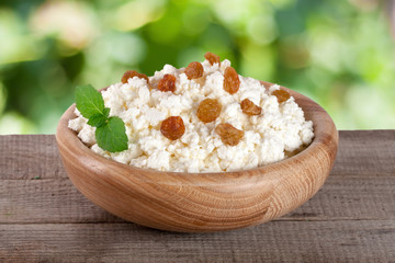Cottage cheese in a wooden bowl on board with blurred garden background